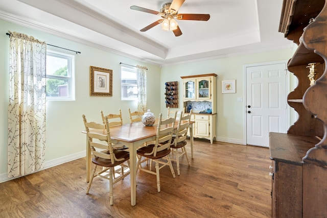 dining space featuring a raised ceiling, wood finished floors, crown molding, baseboards, and ceiling fan
