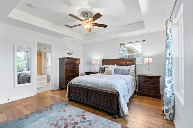 bedroom with ensuite bathroom, visible vents, baseboards, wood finished floors, and a raised ceiling