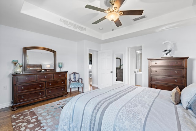 bedroom featuring a tray ceiling, visible vents, baseboards, wood finished floors, and ceiling fan
