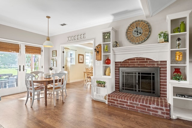 dining area featuring wood finished floors, visible vents, ornamental molding, french doors, and a brick fireplace