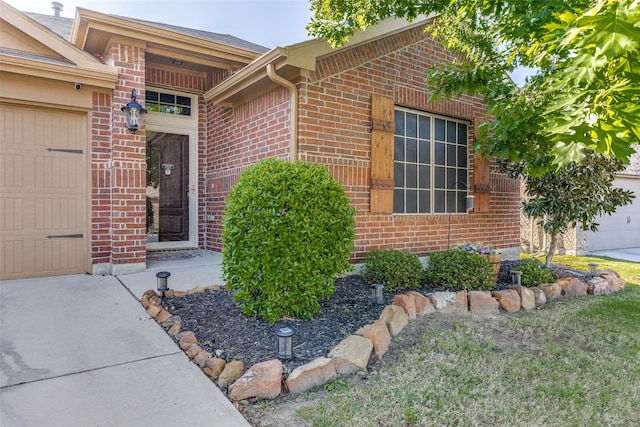 view of exterior entry featuring brick siding, driveway, and a garage