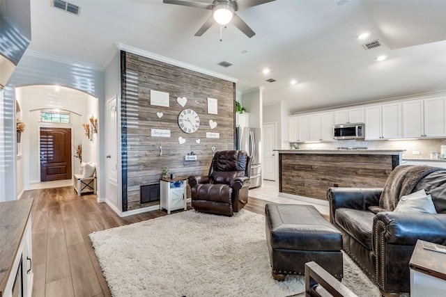 living area with ceiling fan, visible vents, and ornamental molding