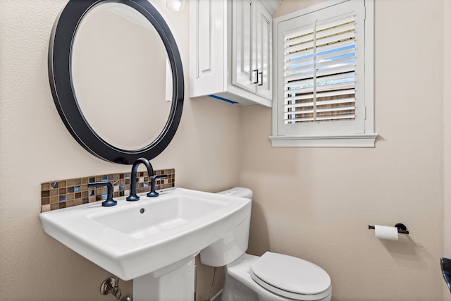 half bath with backsplash, toilet, and a sink