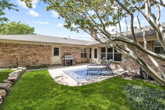 back of property with a lawn, brick siding, roof with shingles, and a patio