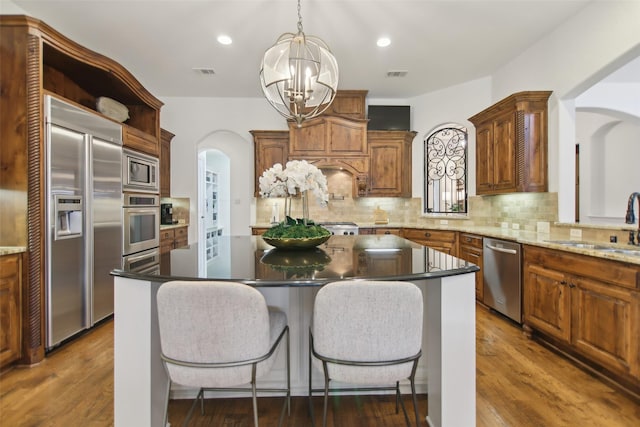 kitchen with arched walkways, built in appliances, a sink, visible vents, and a notable chandelier