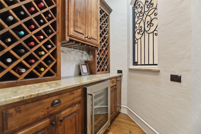 wine cellar featuring beverage cooler, wood finished floors, a bar, and baseboards