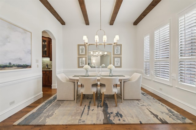 dining area featuring beamed ceiling, an inviting chandelier, wood finished floors, and arched walkways