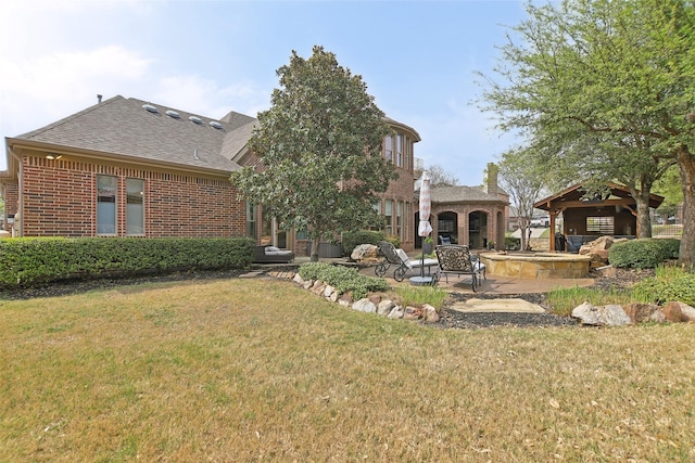 back of house with a patio, brick siding, a yard, and roof with shingles