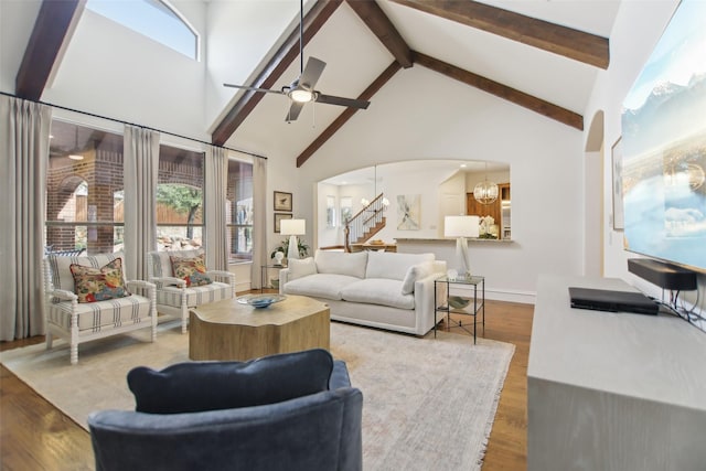 living room with arched walkways, wood finished floors, stairs, ceiling fan, and high vaulted ceiling