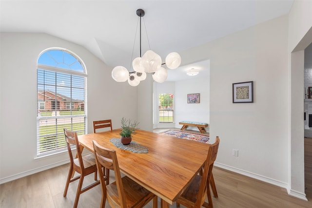 dining area featuring light wood-type flooring, vaulted ceiling, baseboards, and a chandelier