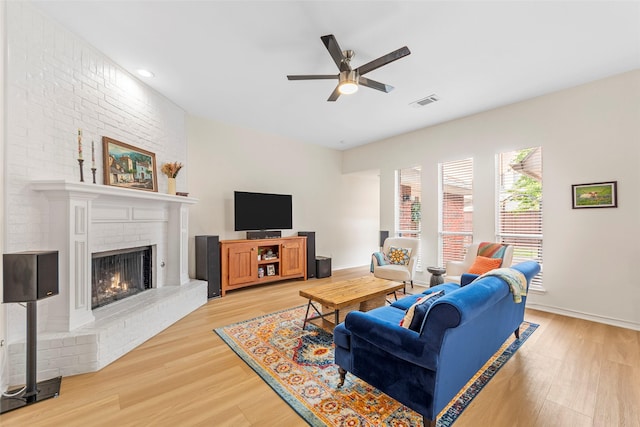 living room with a ceiling fan, light wood-style floors, baseboards, a brick fireplace, and visible vents