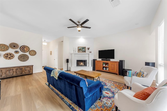 living room featuring a fireplace, light wood-style floors, visible vents, and ceiling fan