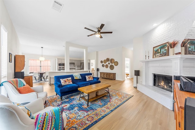 living room featuring light wood finished floors, a ceiling fan, visible vents, and a fireplace