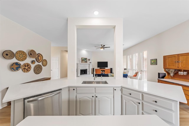 kitchen featuring a peninsula, stainless steel dishwasher, a sink, a ceiling fan, and a fireplace