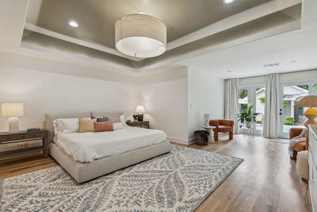 bedroom with wood finished floors, access to exterior, visible vents, and a raised ceiling