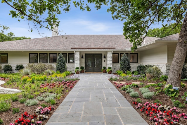 view of front of home featuring french doors, roof with shingles, stone siding, and a chimney
