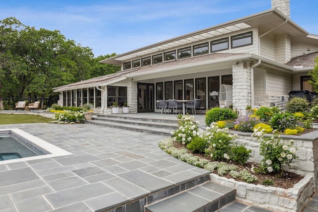 rear view of property with stone siding, uncovered parking, a chimney, and a patio