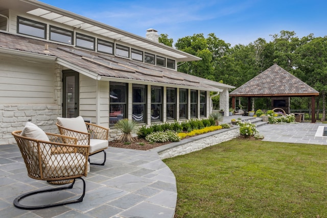 rear view of house with a gazebo, stone siding, a chimney, a patio area, and a lawn