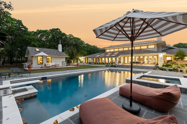 pool at dusk with an exterior structure, an in ground hot tub, a patio, an outdoor structure, and an outdoor pool