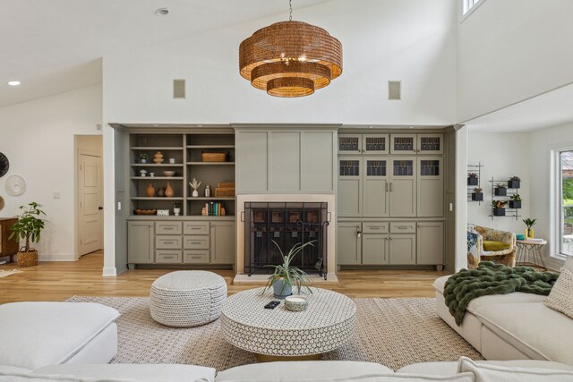 living area with recessed lighting, light wood-style flooring, a fireplace with raised hearth, and high vaulted ceiling