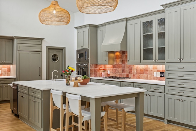 kitchen featuring stainless steel appliances, custom exhaust hood, backsplash, gray cabinetry, and a breakfast bar