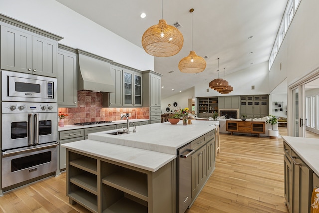kitchen with wall chimney exhaust hood, a sink, gray cabinets, high vaulted ceiling, and appliances with stainless steel finishes