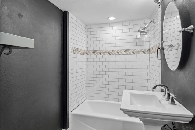 full bath featuring a textured wall, a sink, and shower / bath combination