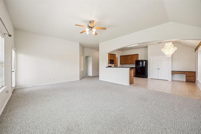 unfurnished living room featuring vaulted ceiling, ceiling fan with notable chandelier, arched walkways, light colored carpet, and baseboards