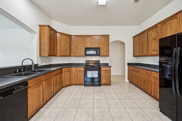 kitchen with brown cabinets, dark countertops, a sink, arched walkways, and black appliances