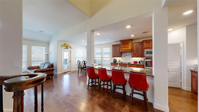 916 Sunset Haven Dr, Little Elm, TX 75068 - kitchen featuring stainless steel appliances, a kitchen breakfast bar, dark wood-style floors, custom range hood, and open floor plan