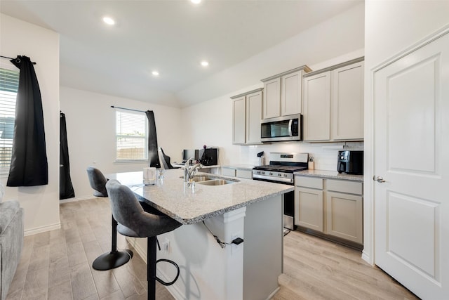 kitchen featuring light wood-type flooring, stainless steel appliances, a kitchen island with sink, and a sink