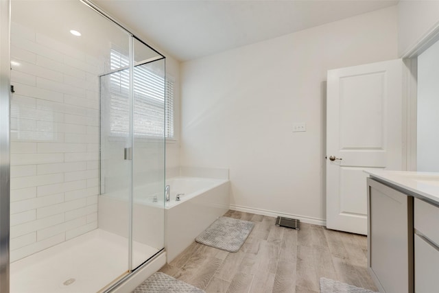 bathroom featuring a shower stall, a garden tub, wood finished floors, vanity, and baseboards