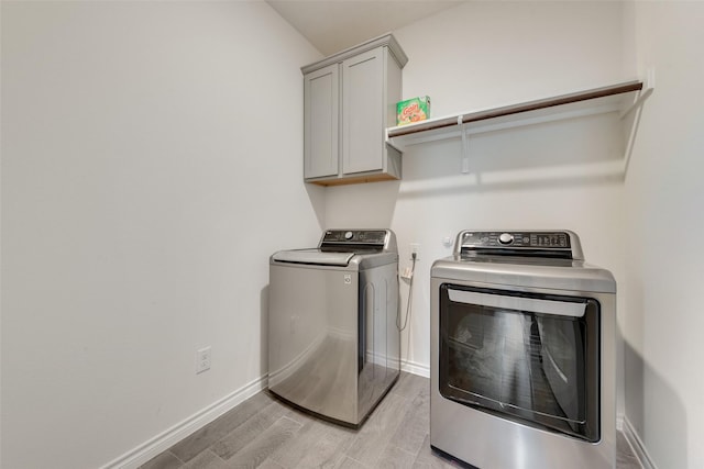clothes washing area featuring cabinet space, washing machine and dryer, baseboards, and light wood-style flooring