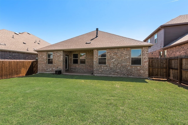 back of house with a fenced backyard, roof with shingles, brick siding, and a yard