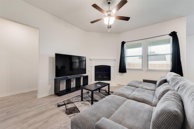 living room featuring a fireplace, light wood-style floors, baseboards, and ceiling fan