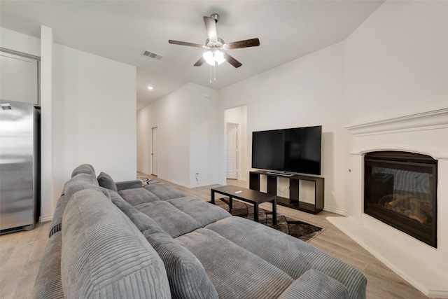 living room featuring visible vents, a ceiling fan, light wood-style floors, baseboards, and a glass covered fireplace