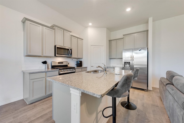 kitchen with a sink, light wood-style floors, gray cabinets, a kitchen bar, and appliances with stainless steel finishes