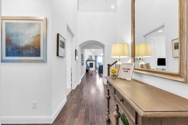 hallway featuring baseboards, a high ceiling, arched walkways, and dark wood-type flooring