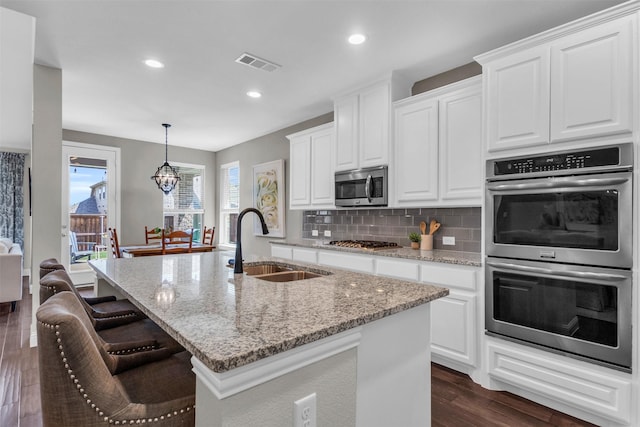 kitchen featuring a sink, appliances with stainless steel finishes, backsplash, dark wood-style flooring, and visible vents