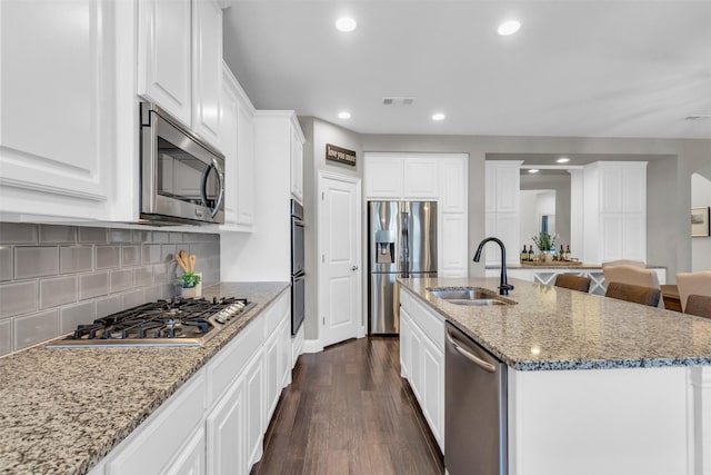 kitchen with white cabinets, dark wood finished floors, a sink, a kitchen island with sink, and appliances with stainless steel finishes
