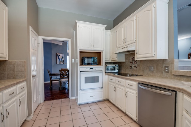 kitchen featuring tasteful backsplash, white cabinetry, under cabinet range hood, tile countertops, and black appliances