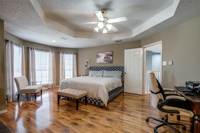 bedroom with a tray ceiling, wood finished floors, a textured ceiling, and visible vents