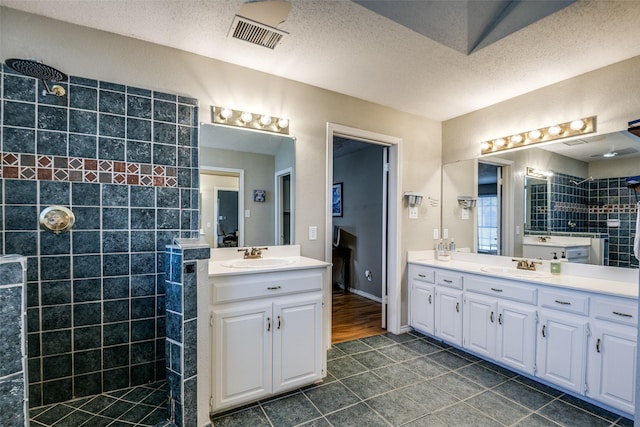 full bath featuring two vanities, visible vents, a sink, and a walk in shower