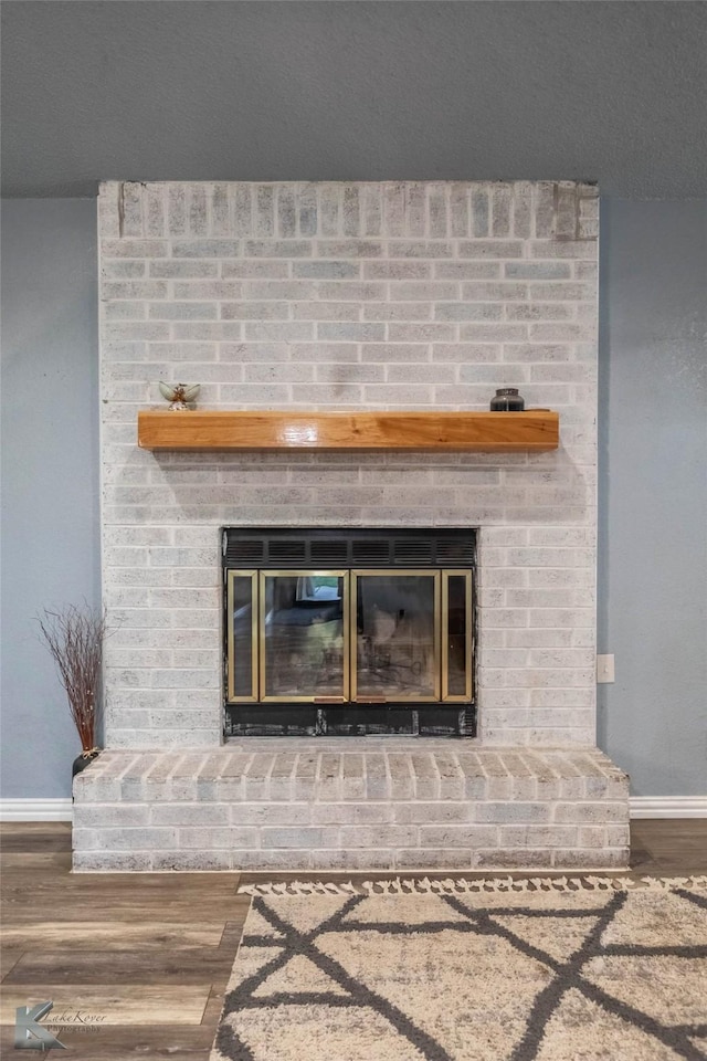 interior details featuring wood finished floors, a brick fireplace, and baseboards