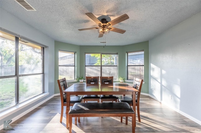 dining space with a ceiling fan, wood finished floors, a textured ceiling, baseboards, and visible vents