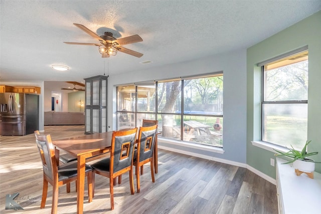 dining space with ceiling fan, baseboards, a textured ceiling, and light wood-type flooring