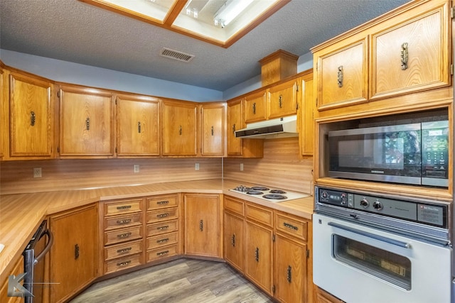 kitchen with visible vents, white appliances, brown cabinets, light countertops, and under cabinet range hood