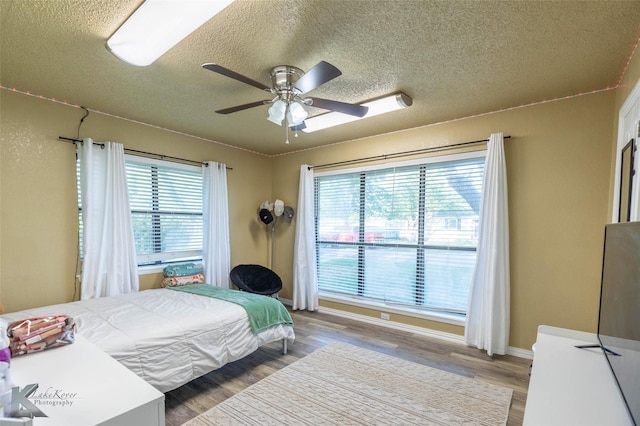 bedroom with wood finished floors, a textured ceiling, ceiling fan, and multiple windows