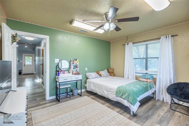 bedroom featuring baseboards, wood finished floors, visible vents, and a textured ceiling