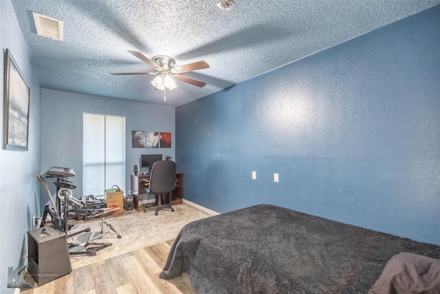 bedroom featuring a ceiling fan, wood finished floors, visible vents, and a textured ceiling